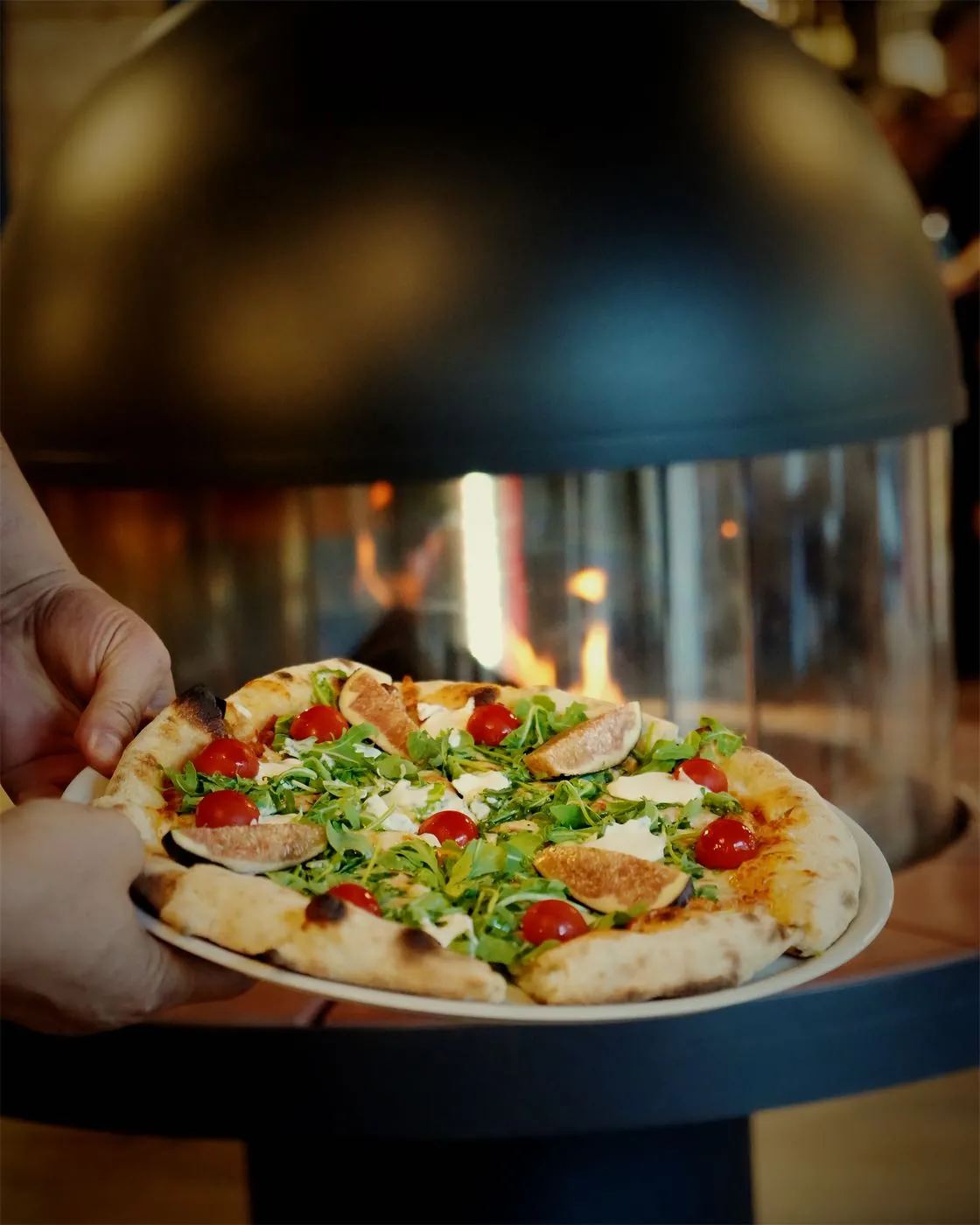Une pizza sortie du four, présentée devant le feu